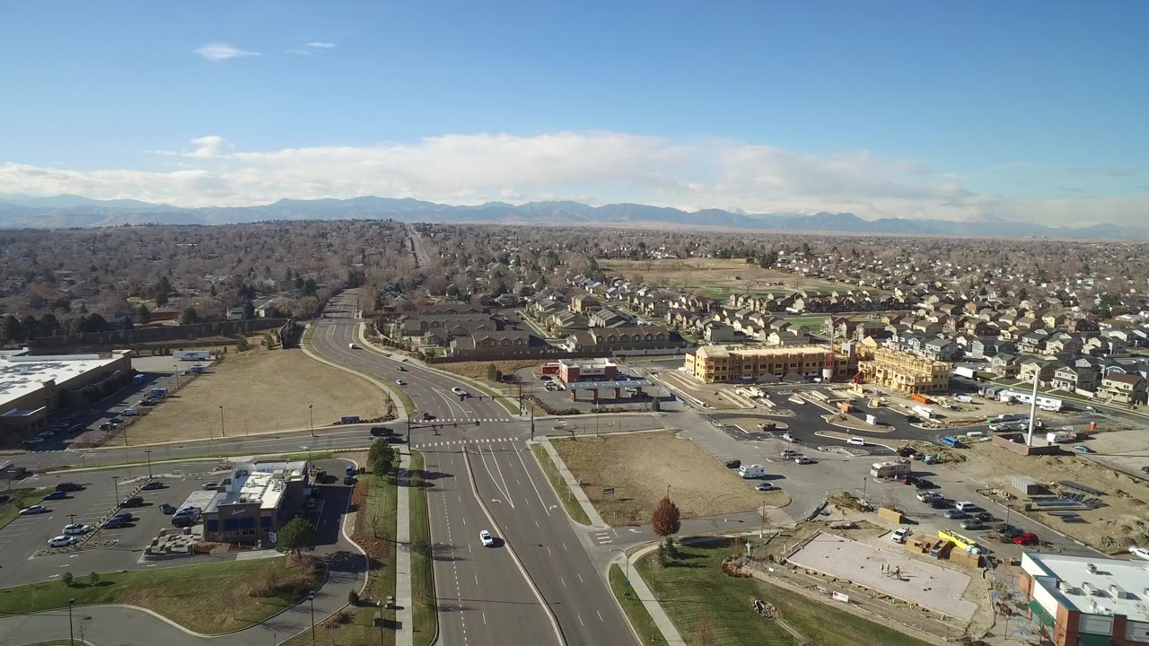 Aerial view over open lots, a curved road, homes, and mountain horizon.