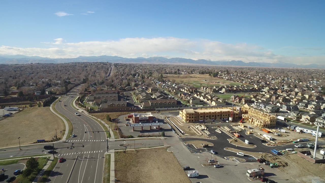 Aerial view of a suburban road intersection, construction site, houses, and distant mountains.