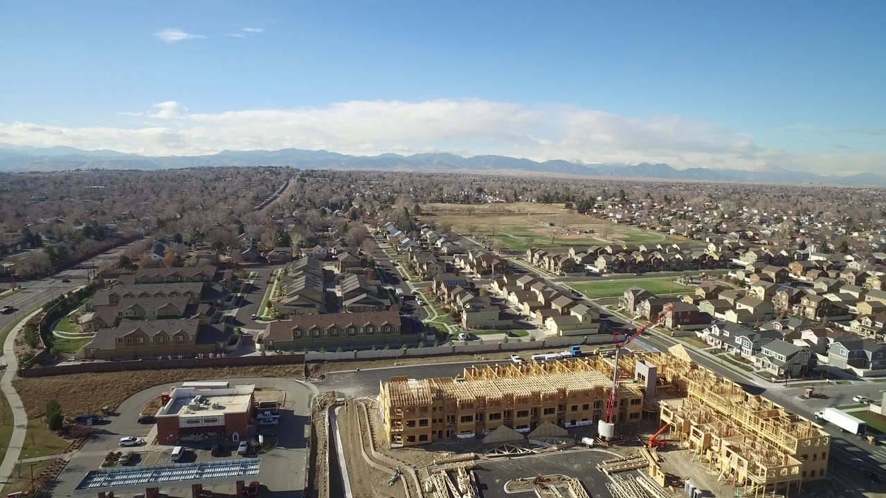 Drone-height view over new construction beside suburban streets and houses.