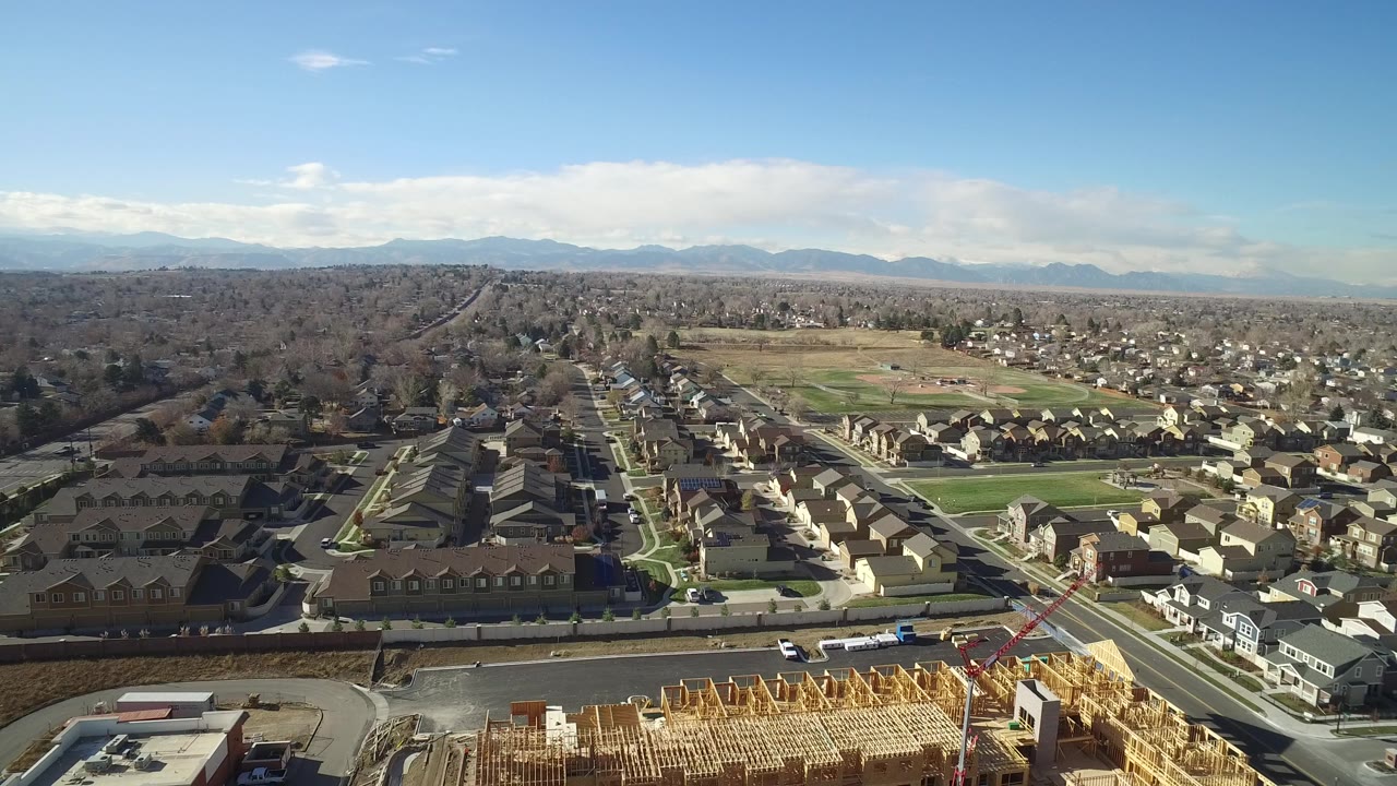Aerial view of a wood-frame construction site beside roads and suburban homes.