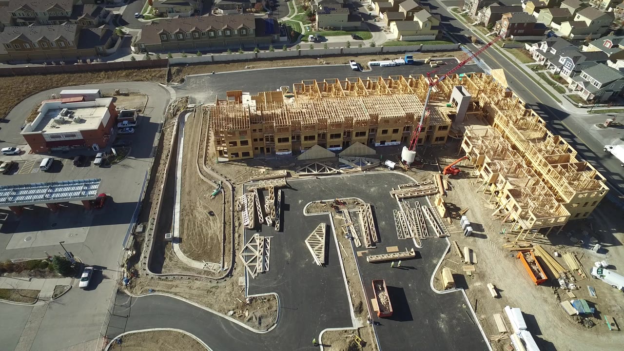 Aerial view of wood-framed construction beside suburban roads and homes.