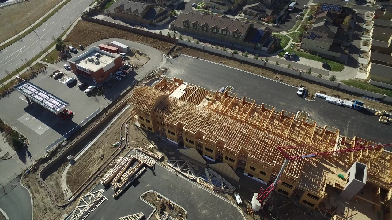 High aerial frame over Hidden Lake, Colorado showing a long wood-framed building under construction, paved roads, nearby houses, parked vehicles, and no visible people.