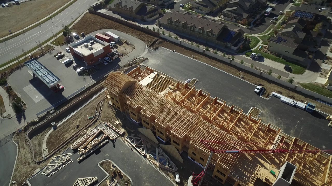 High-angle Hidden Lake, Colorado frame showing the construction site running across the lower right, residential roofs in the background, broad roads, parked vehicles, and no visible people.