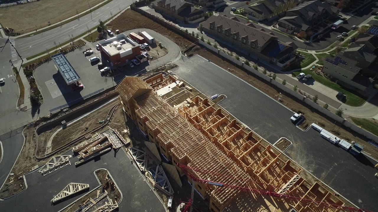 Aerial frame of wood construction next to a curved street and parked vehicles.
