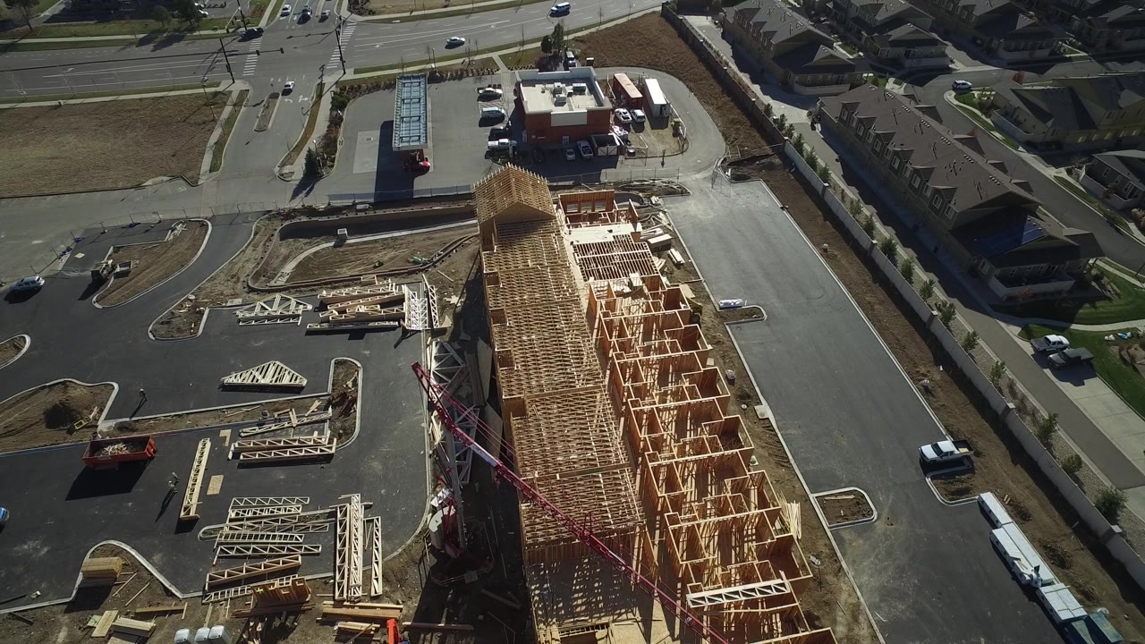 Drone view of a roadside construction site with stacked wood trusses and traffic nearby.