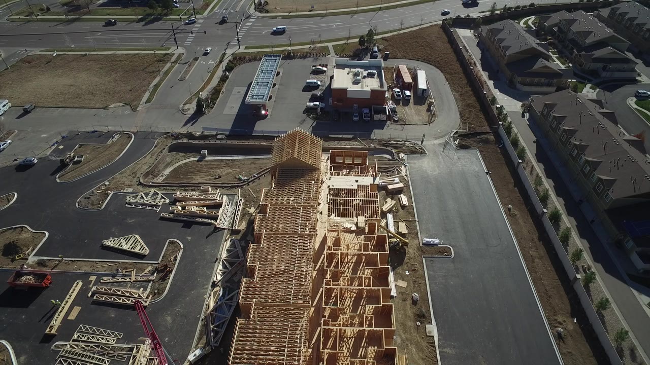 Aerial view of a timber-framed construction site beside roads and parking lots.