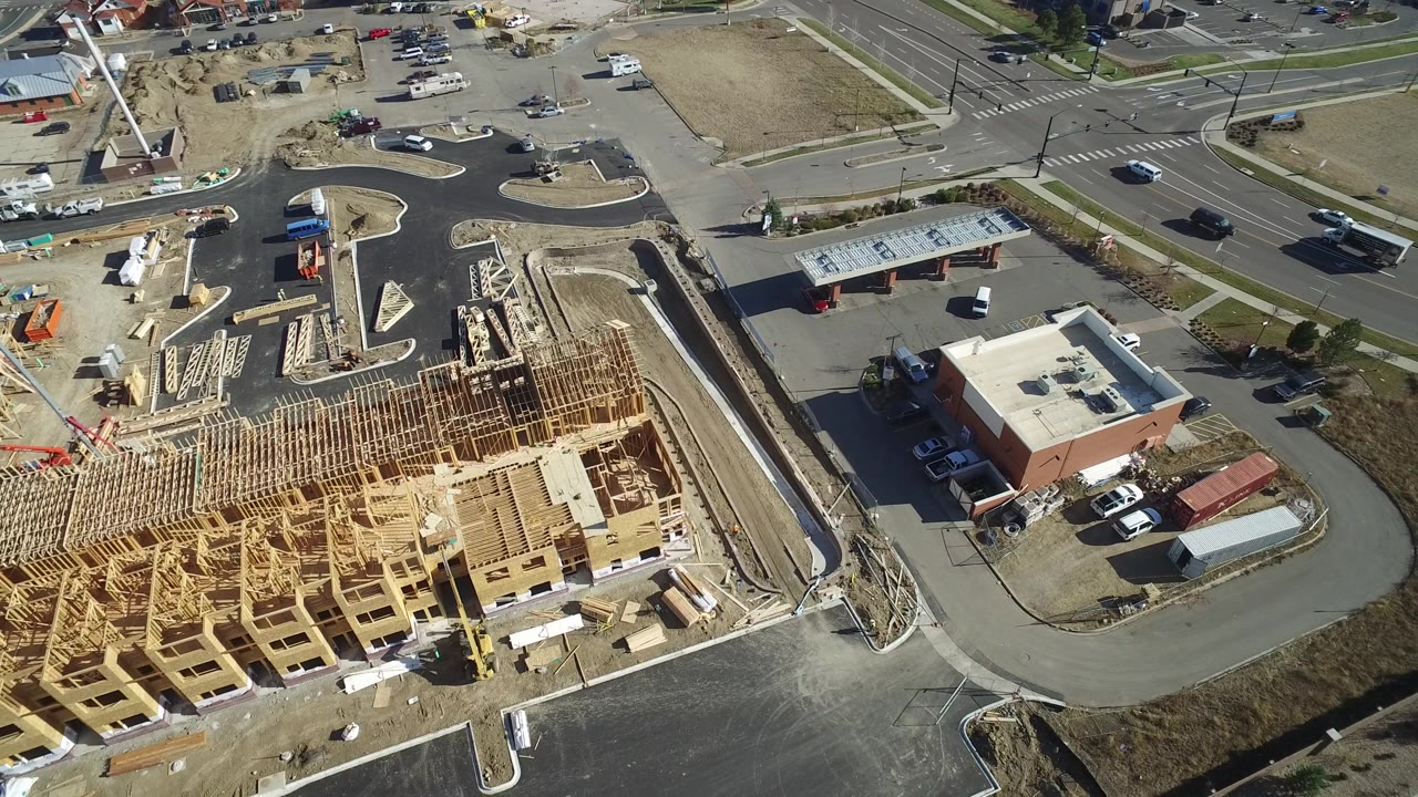 Aerial construction site with cranes or lifts, framed buildings, and surrounding roads.