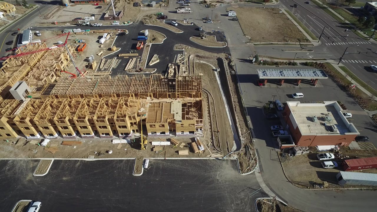 Birdseye view over a Hidden Lake, Colorado residential construction site with exposed wood framing, blacktop parking areas, nearby roads, and no visible people.