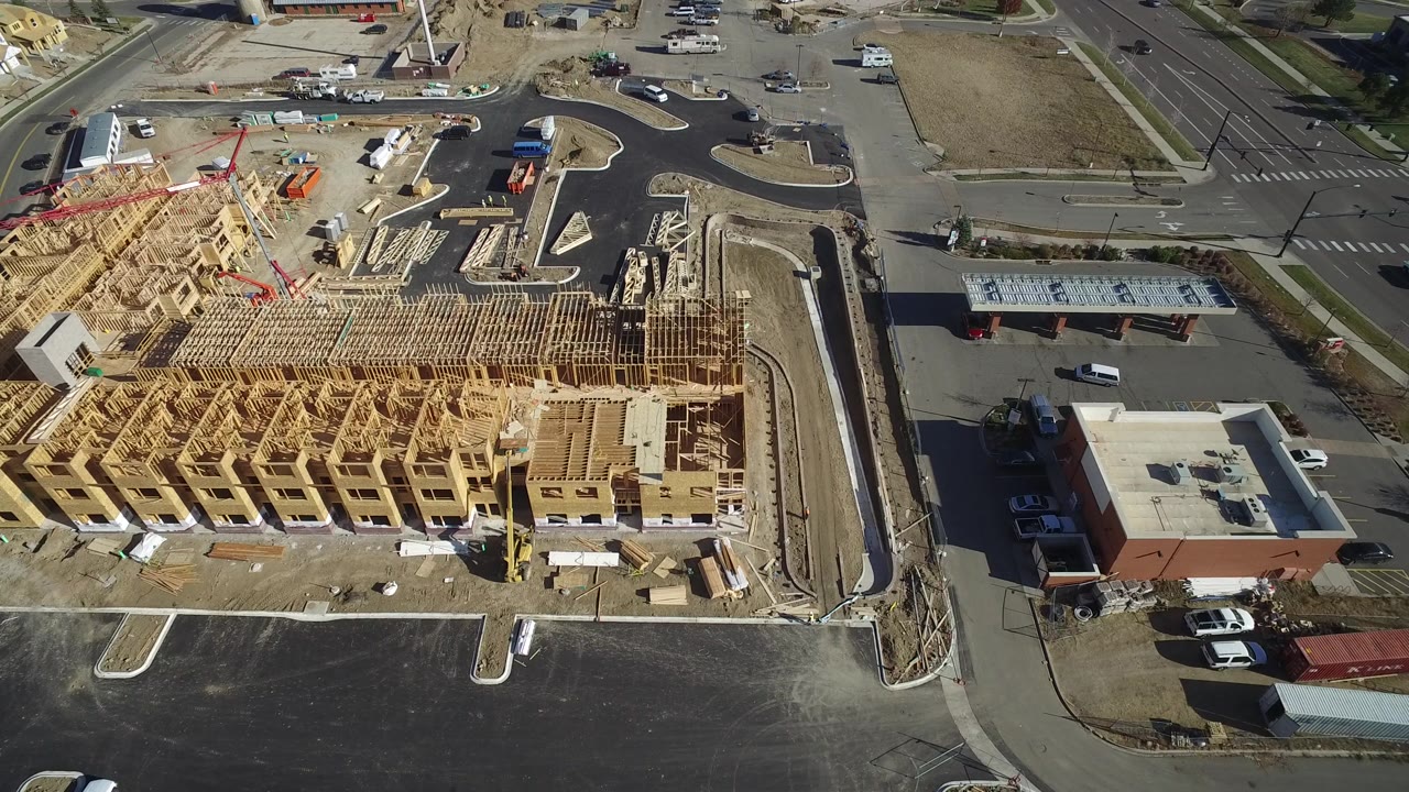 Drone view of a large timber-framed housing block with roads and a commercial-looking low building nearby.