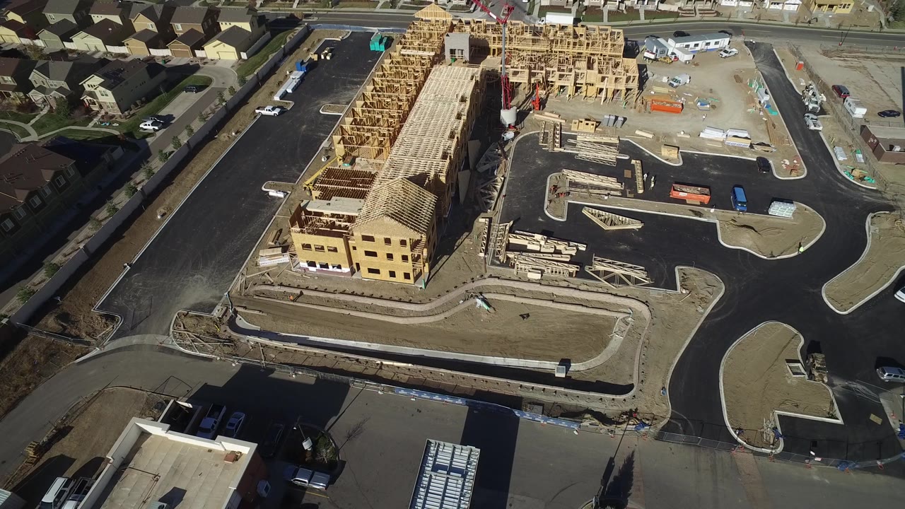 Aerial frame in Hidden Lake, Colorado showing a red crane beside wood framing, curved streets, construction materials, nearby homes, and no visible people.