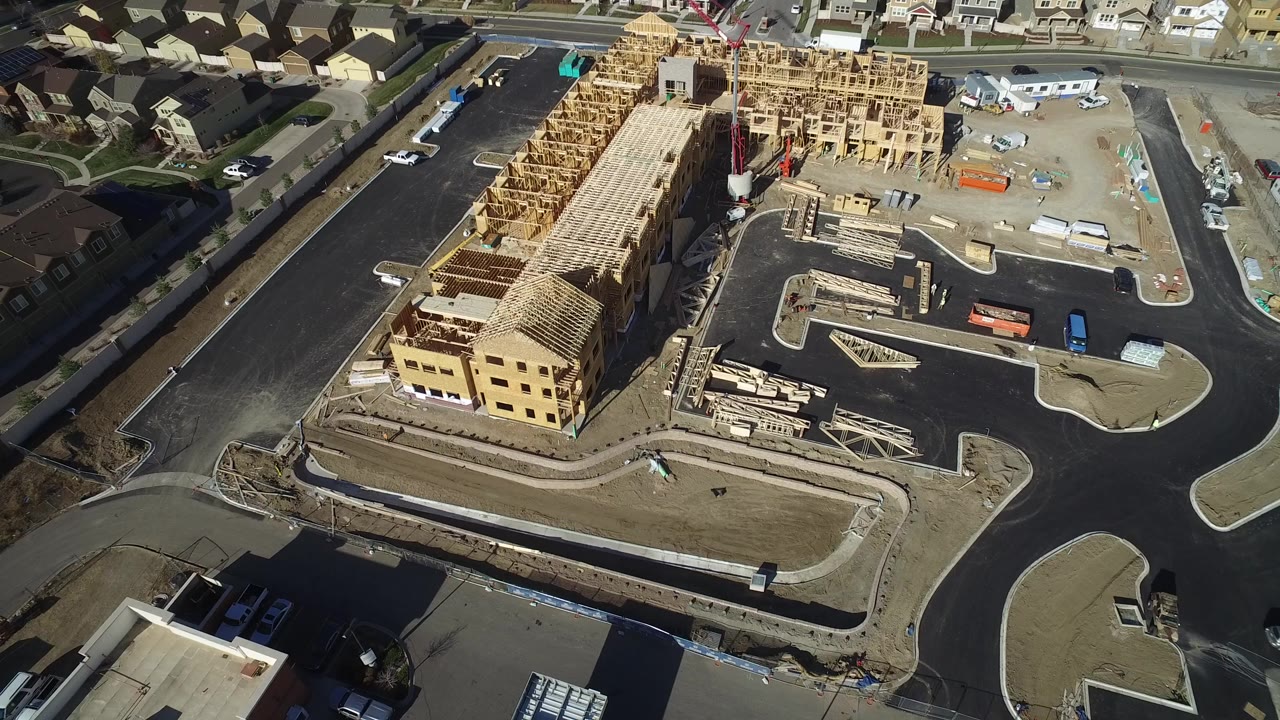 Aerial construction site with framed building, streets, and surrounding homes.