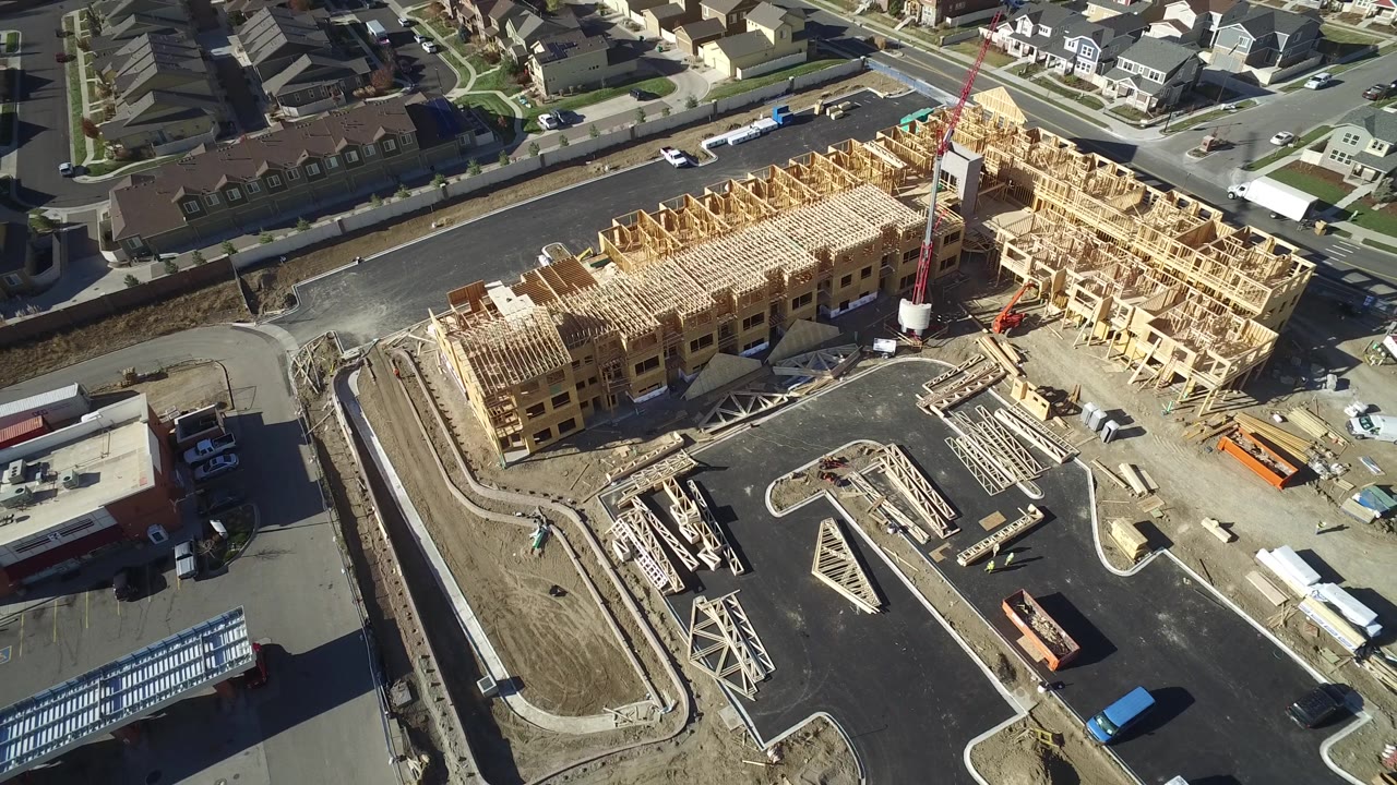 Aerial shot of new wood framing with a paved lot and nearby commercial-looking building.