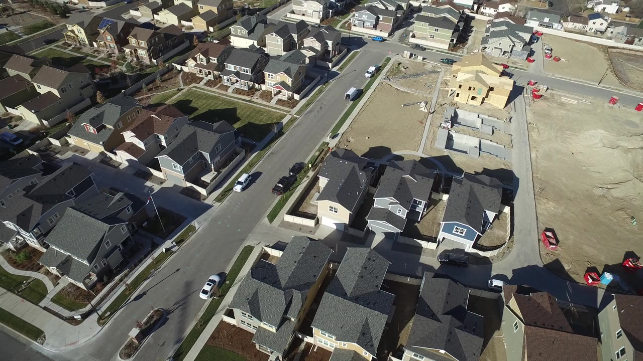 Aerial frame over Hidden Lake, Colorado showing finished houses, a paved street, parked cars, bare construction lots, and no visible people.