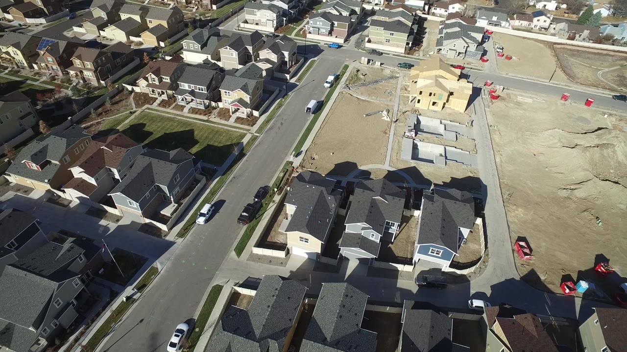 Drone-like view of rooftops and a large graded dirt parcel.