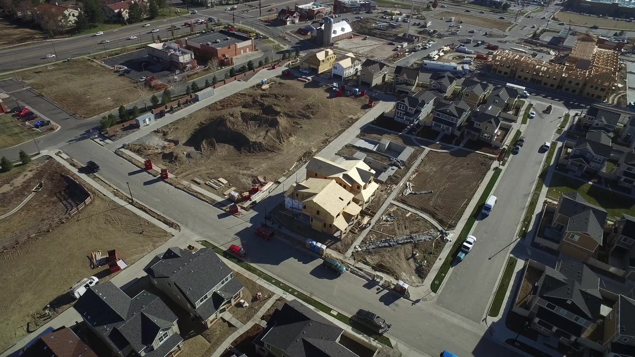 Aerial view in Hidden Lake, Colorado with dark-roofed homes in the foreground, pale framed houses near the center, dirt lots, and no clearly visible people.