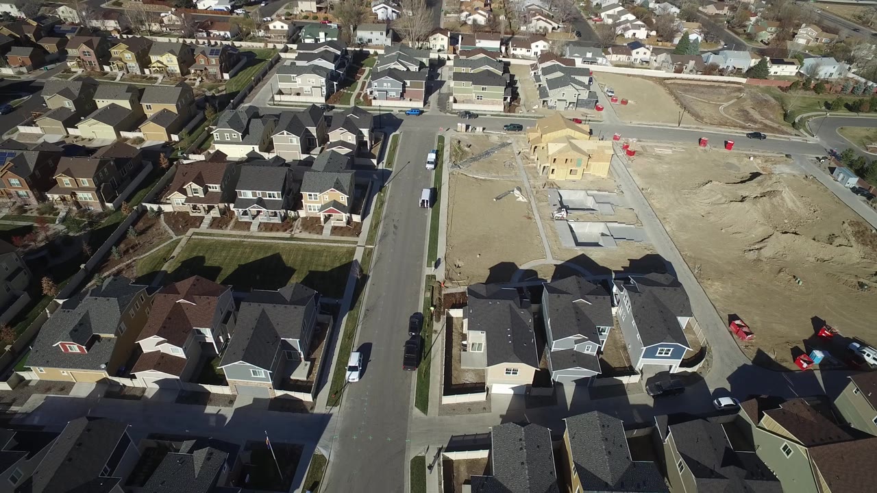 Overhead frame of Hidden Lake, Colorado rooftops and a straight residential road, with unfinished sandy lots beyond the houses and no visible people.