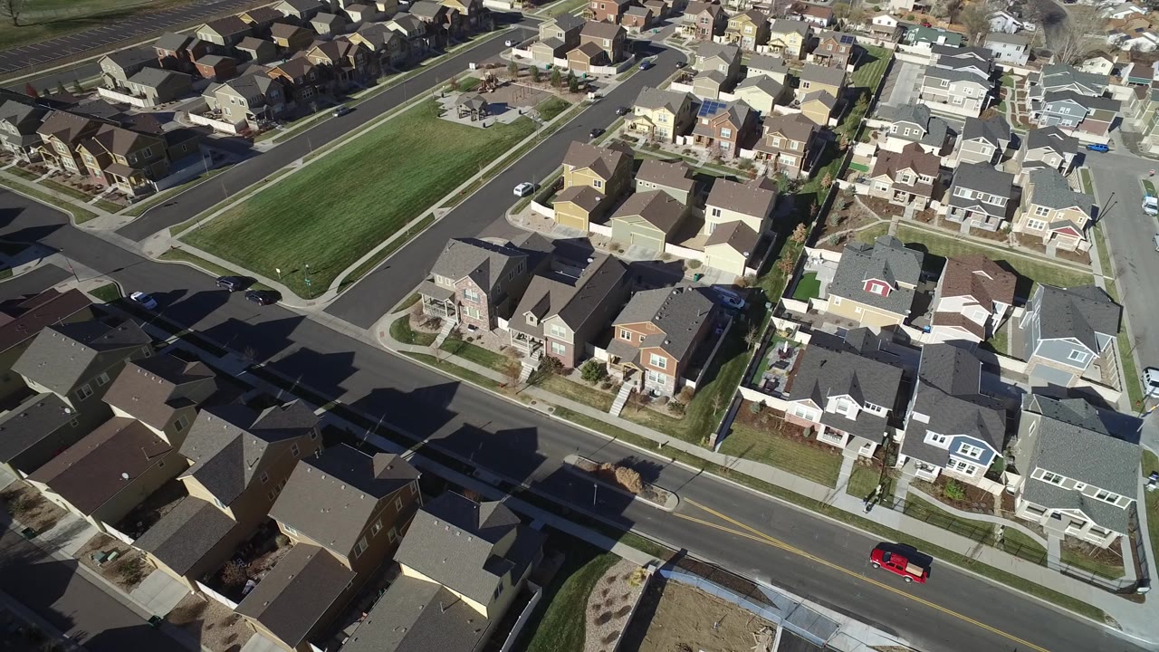 Drone-height view of Hidden Lake, Colorado with large detached homes, driveways, sidewalks, a green rectangular lawn area, and cars along the roads with no visible people.