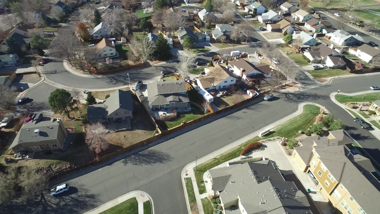 Overhead drone frame in Hidden Lake, Colorado with a wide curved road, clustered homes, fenced backyards, winter-bare trees, and no visible people.