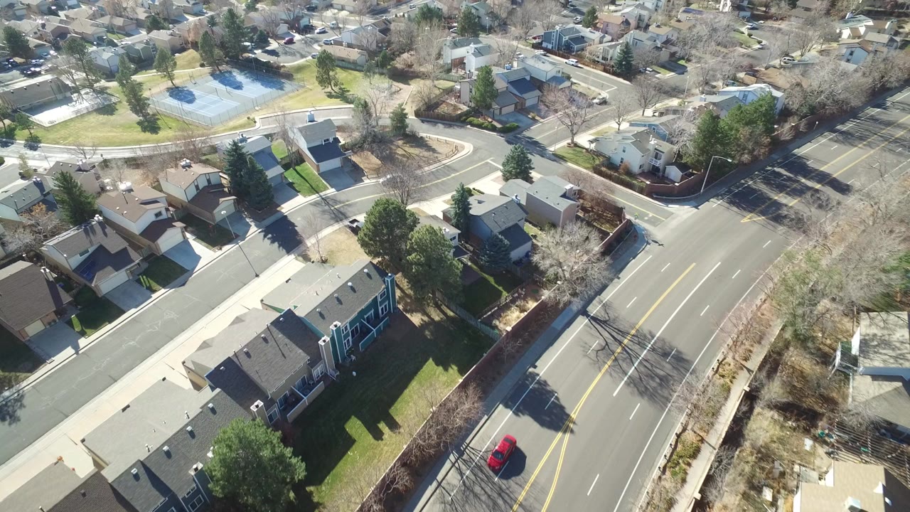 Aerial view over suburban homes, curving roads, lawns, and bare trees.