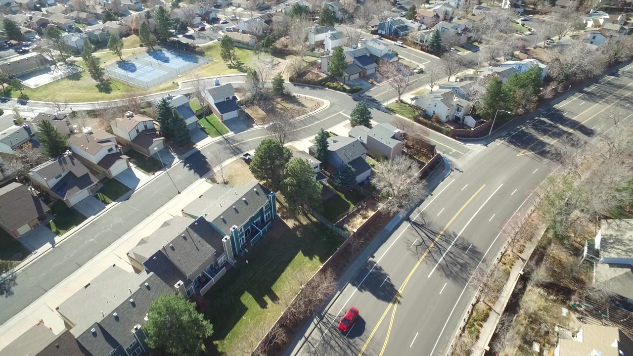 Aerial frame over Hidden Lake, Colorado showing detached houses, a broad paved road, sidewalks, winter trees, and no clearly visible people.