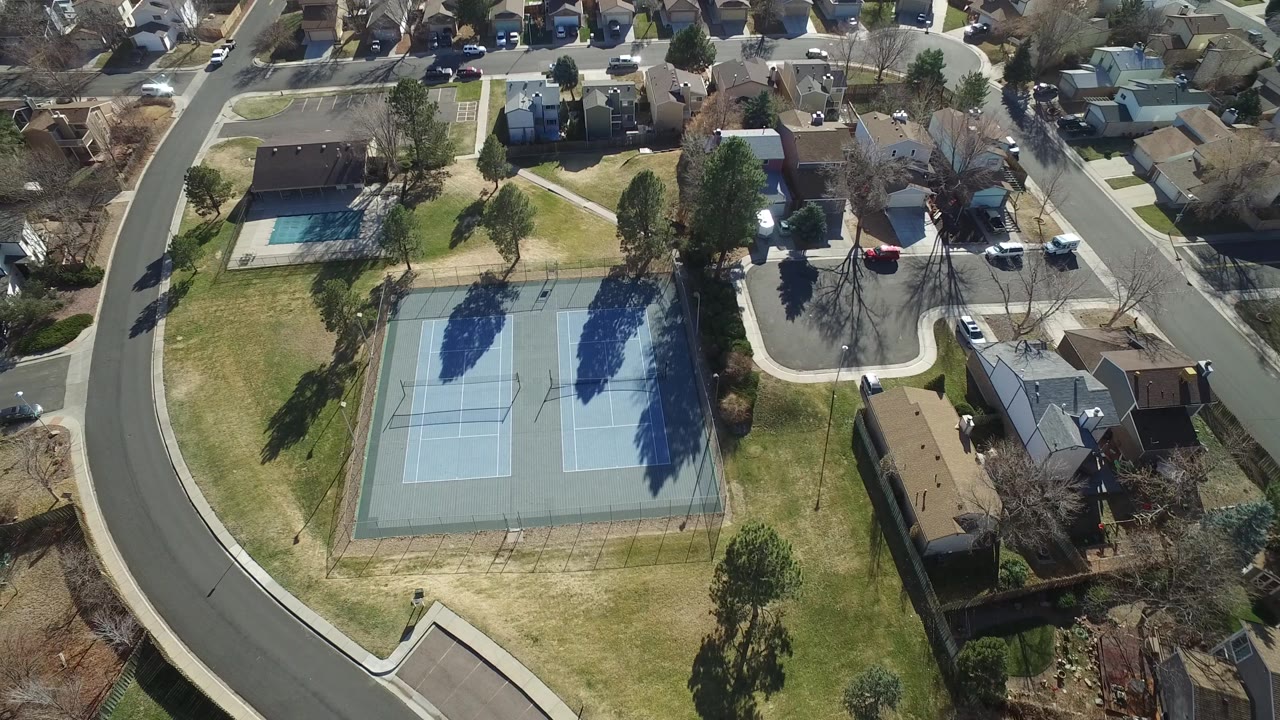 Aerial frame in Hidden Lake, Colorado with the tennis courts centered lower in view, the pool beyond the lawn, houses along the top edge, and no visible people.