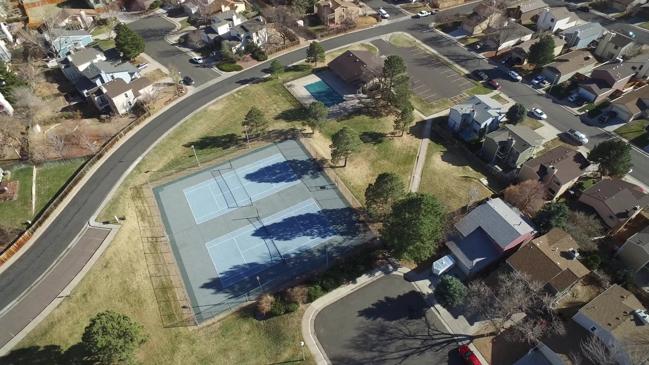 Drone-style view of neighborhood tennis courts, lawns, houses, and roads.