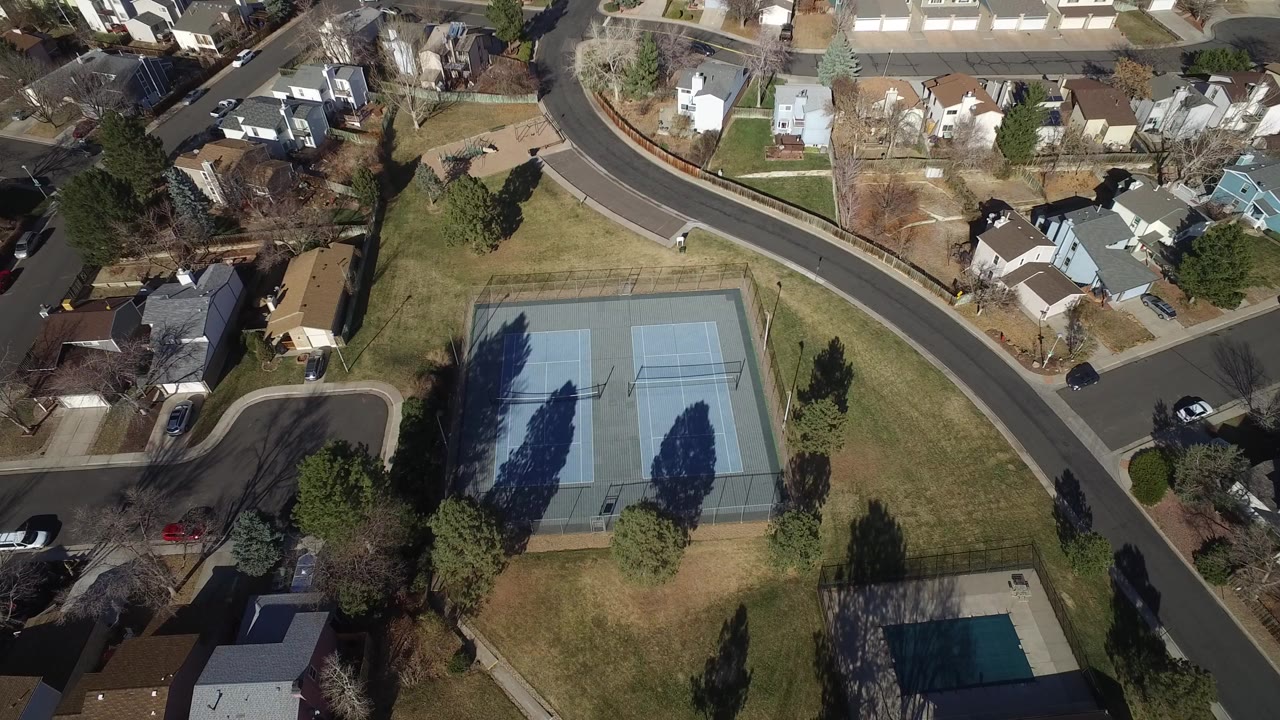 Aerial view of two tennis courts beside suburban homes and curving roads.
