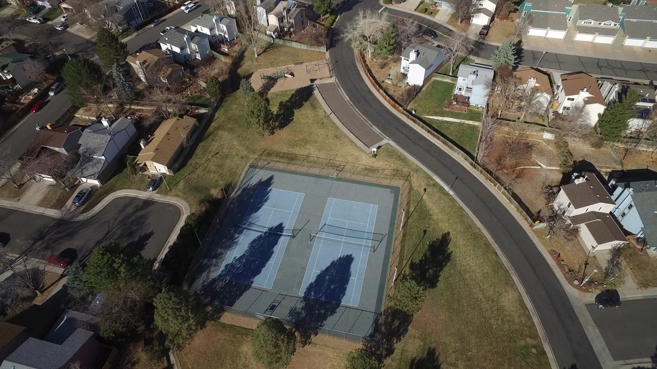 Aerial view of tennis courts beside curved neighborhood streets and homes.