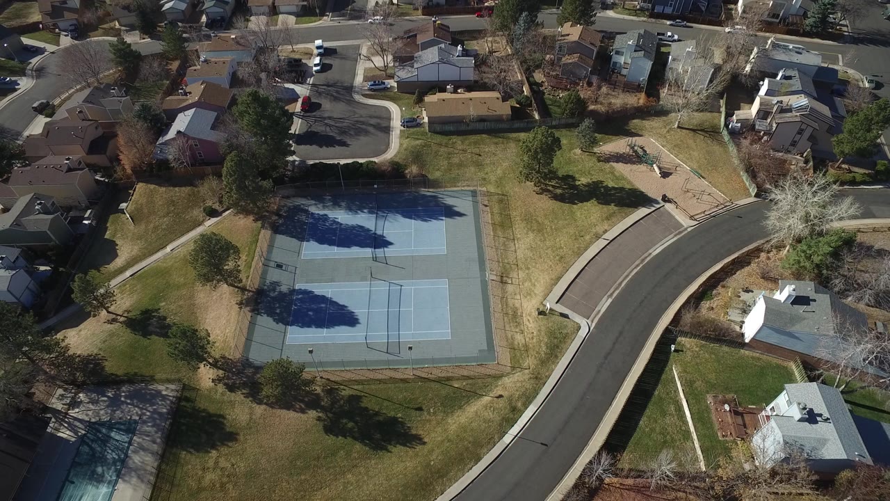 Aerial view in Hidden Lake, Colorado centers the tennis courts with lawns, tree shadows, sidewalks, houses, and no visible people.