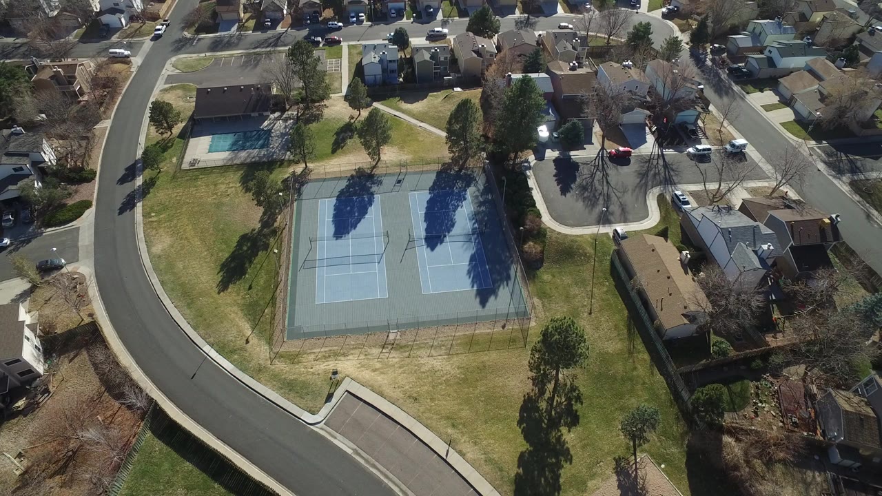 Aerial view of two blue outdoor courts beside a curved neighborhood road
