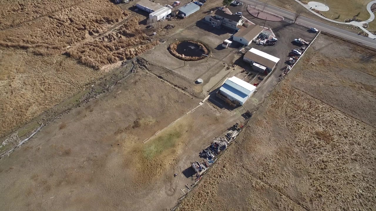 Overhead Hidden Lake, Colorado view with the circular pond near center, pale-roofed sheds, parked trucks and cars, roadside pavement, and no visible people.