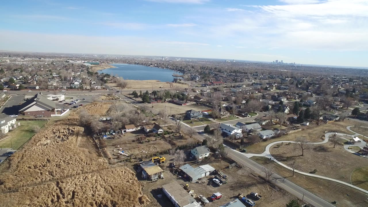 High aerial view of brownfields, homes, roads, and a lake beyond.