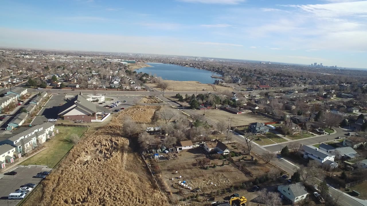 Opening aerial frame over Hidden Lake, Colorado, showing brown brush in the foreground, town buildings and roads below, the lake beyond, and no visible people.