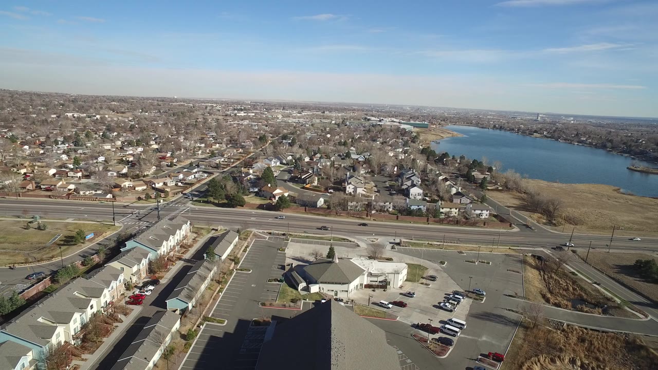 Aerial suburban roadside view with highway, homes, and lake.