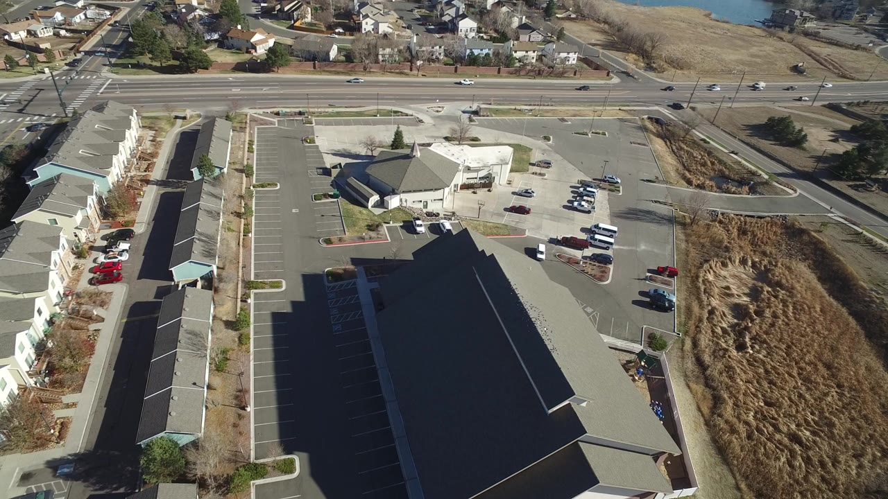 Aerial view of commercial buildings, parking lots, road, and nearby homes.