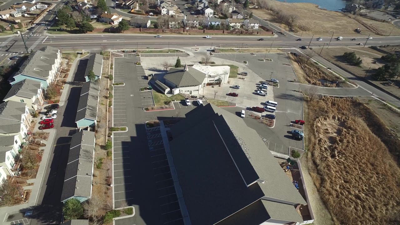 An aerial view in Hidden Lake, Colorado looking down on a long building row, an empty parking area, a road with scattered cars, brown drainage land, and no visible people.