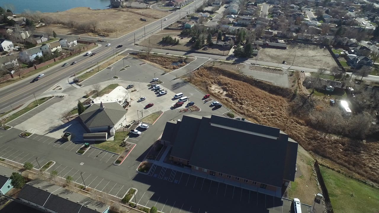 Aerial view of parking lots, commercial roofs, road, houses, and open land.