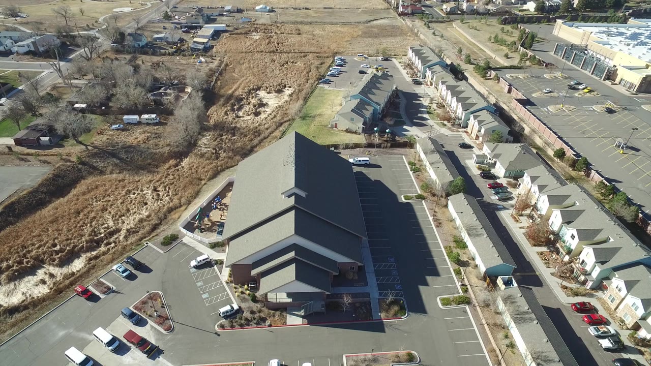 Second overhead frame in Hidden Lake, Colorado with the dark-roofed building centered lower in view, empty parking spaces, a row of homes, and no visible people.