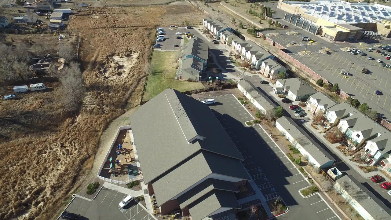 Aerial view of townhouses, parking lots, roads, and a large gray-roofed building.
