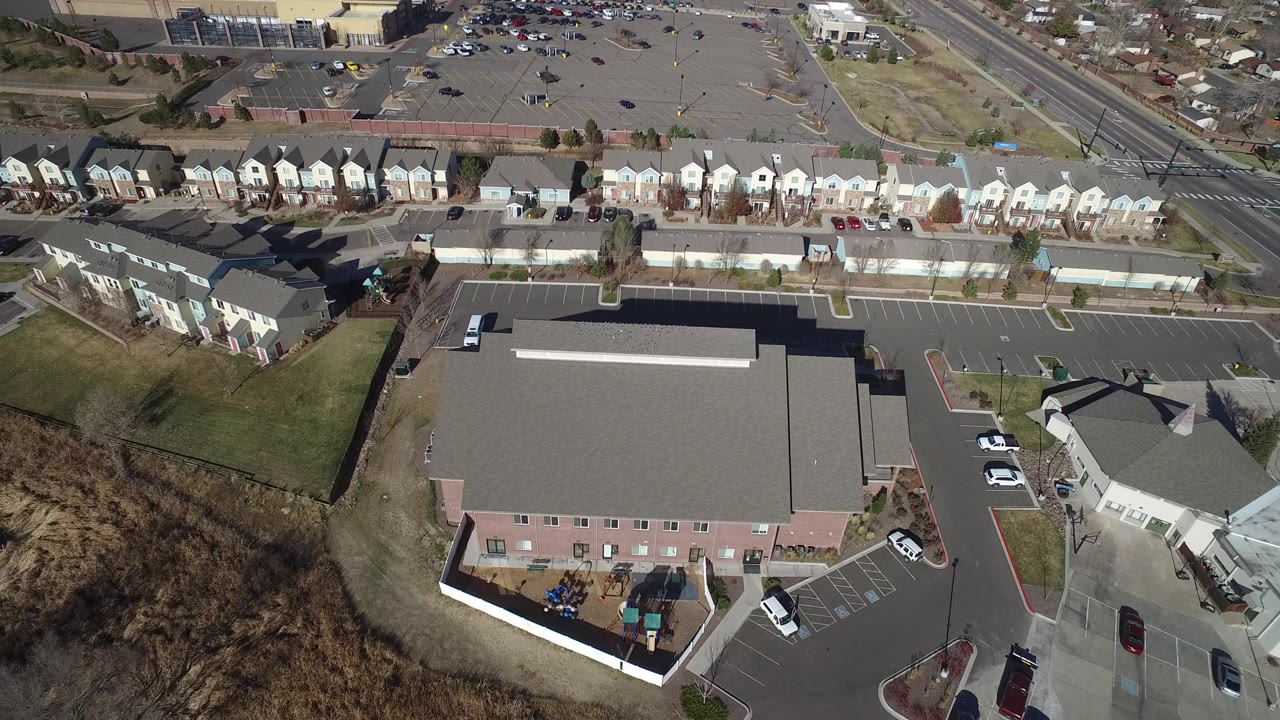 Overhead aerial view in Hidden Lake, Colorado showing a large gray-roofed building, townhouse rows, parking lots, roads, grass strips, and no visible people.