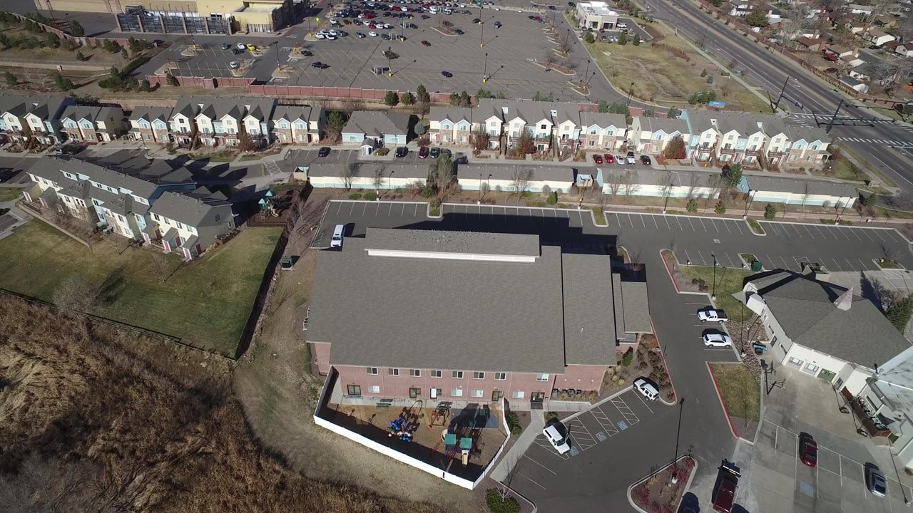 Aerial frame over Hidden Lake, Colorado with the large gray roof centered lower in view, townhouses and a broad parking area above, and no visible people.