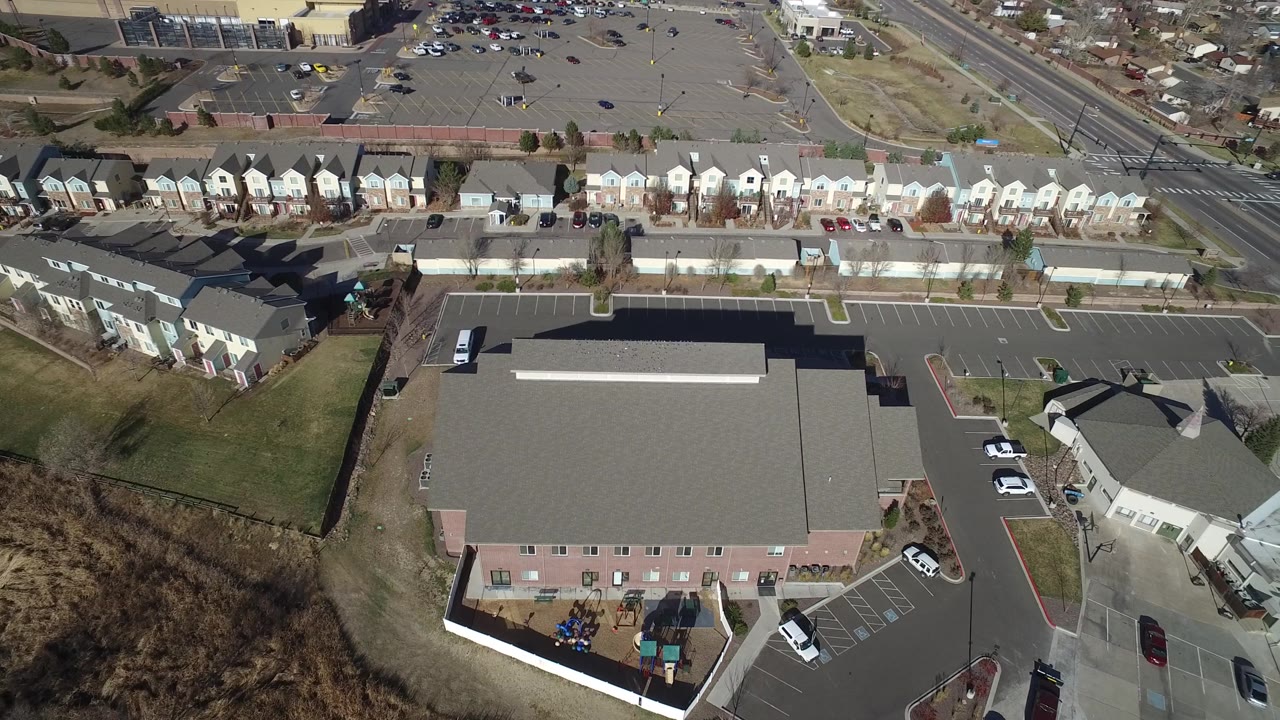 Drone-style overhead view of rooftops, a road intersection, and parking areas.