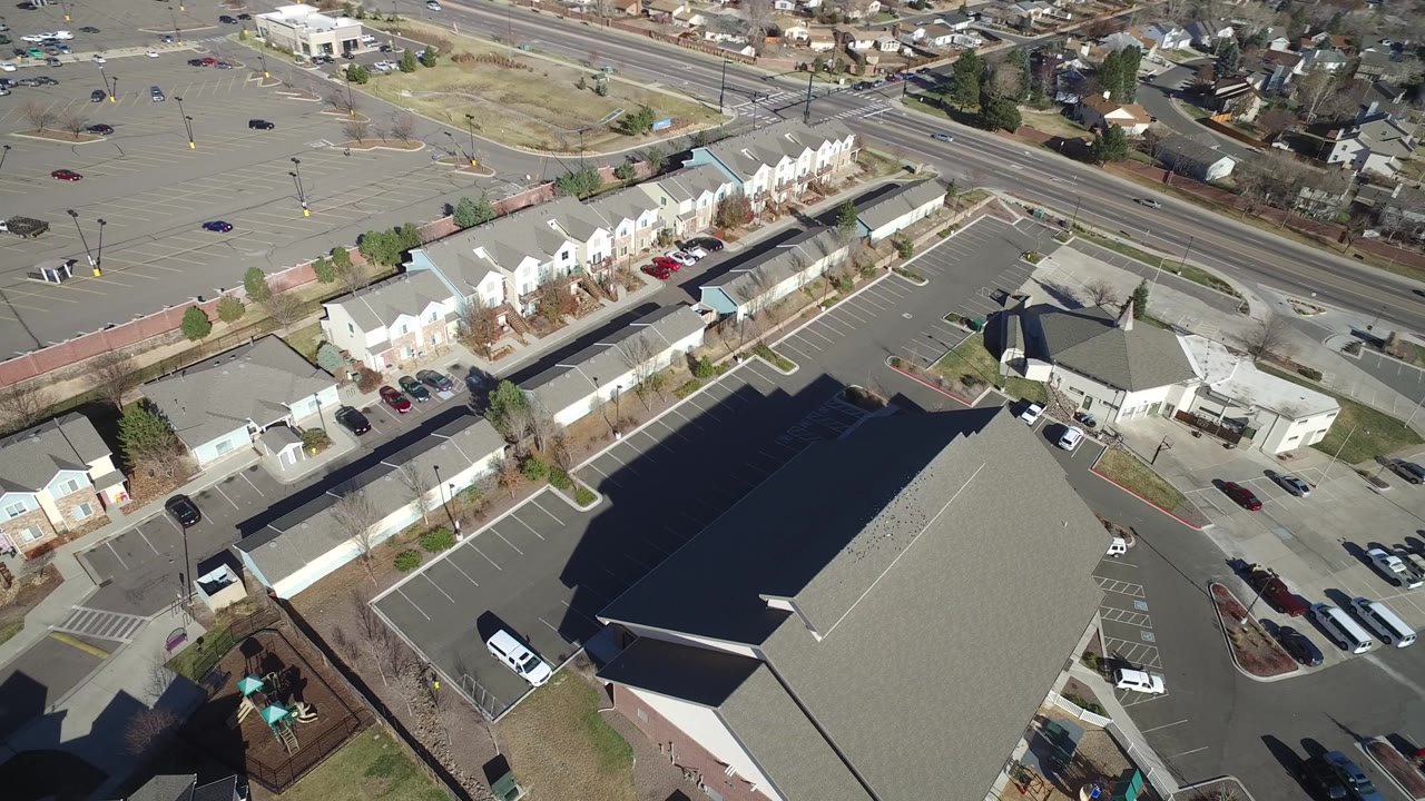 Drone view of residential buildings, parking areas, roads, and dry open ground.