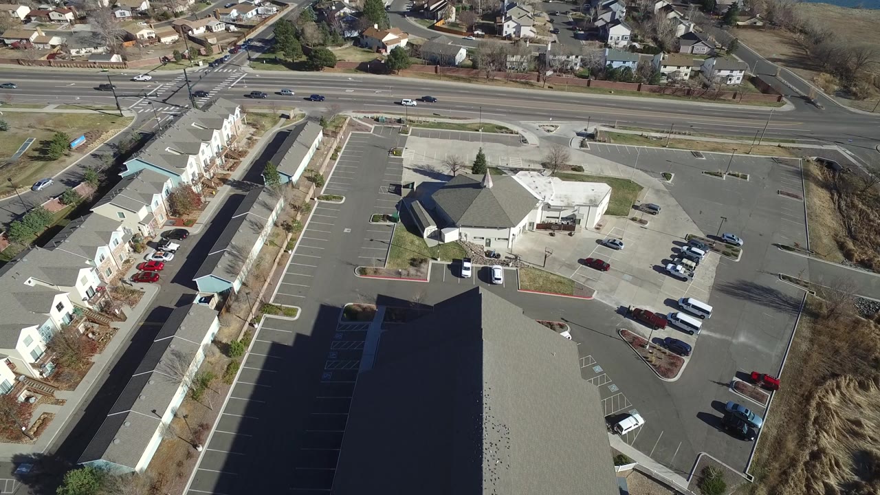 Drone-style view of a parking lot complex with townhomes, a road, and neighboring houses.