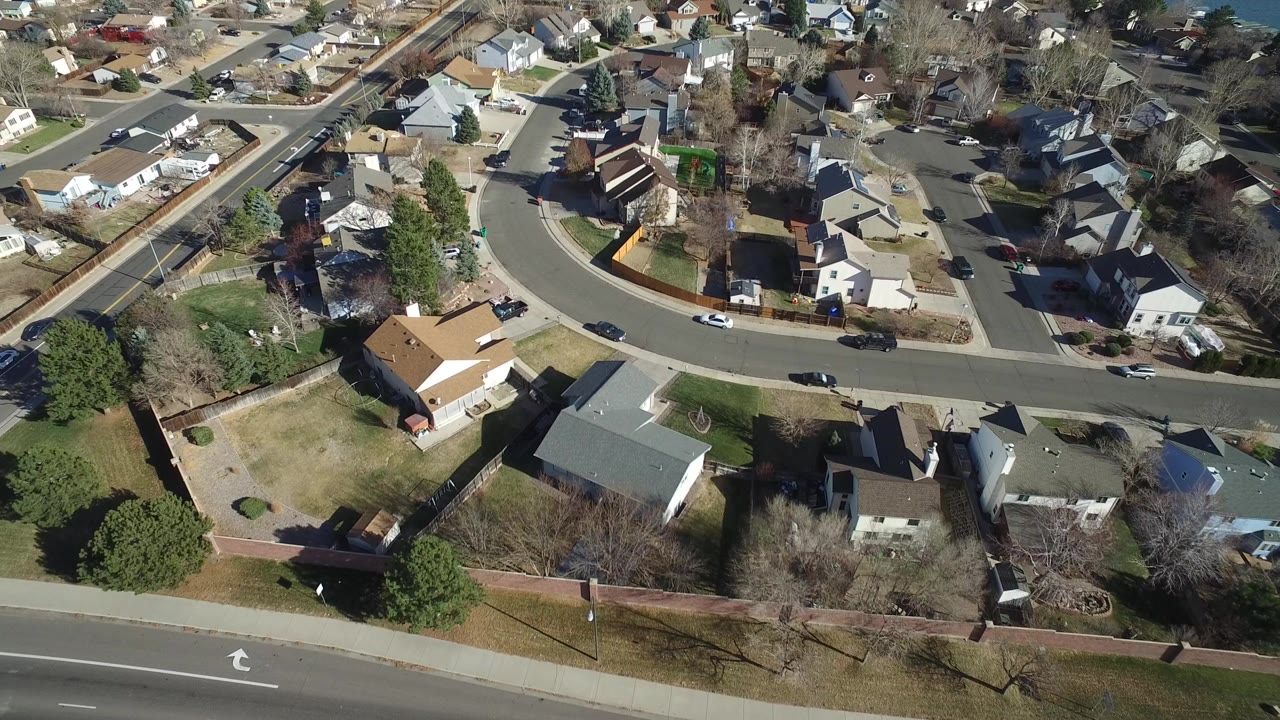 Aerial frame over Hidden Lake, Colorado showing a curved residential street, detached houses, lawns, bare trees, and no visible people.