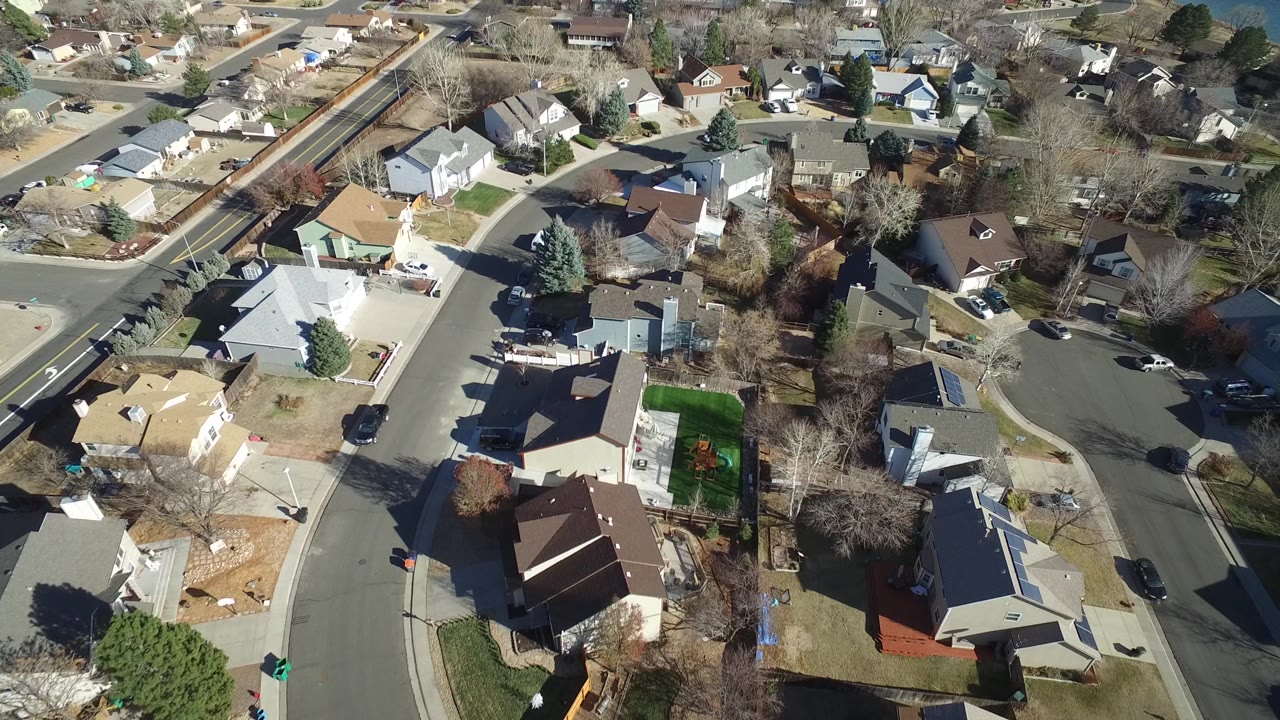 Aerial view in Hidden Lake, Colorado with light-colored houses, brown winter lawns, driveways, parked vehicles, a curved street, and no visible people.