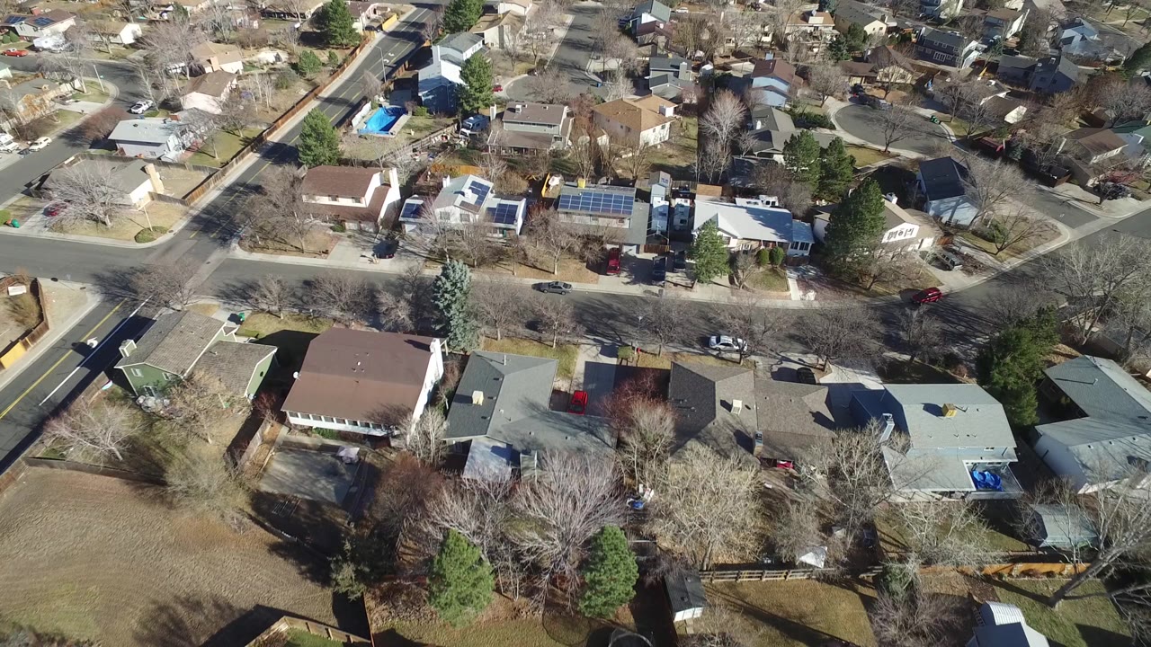 Aerial view in Hidden Lake, Colorado with a bright blue rectangular backyard pool near the upper left, houses, parked vehicles, and bare trees around residential roads.