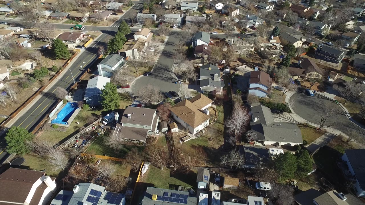 Aerial view in Hidden Lake, Colorado showing detached houses, a curved street, a bright blue backyard pool, parked cars, bare trees, and no visible people.