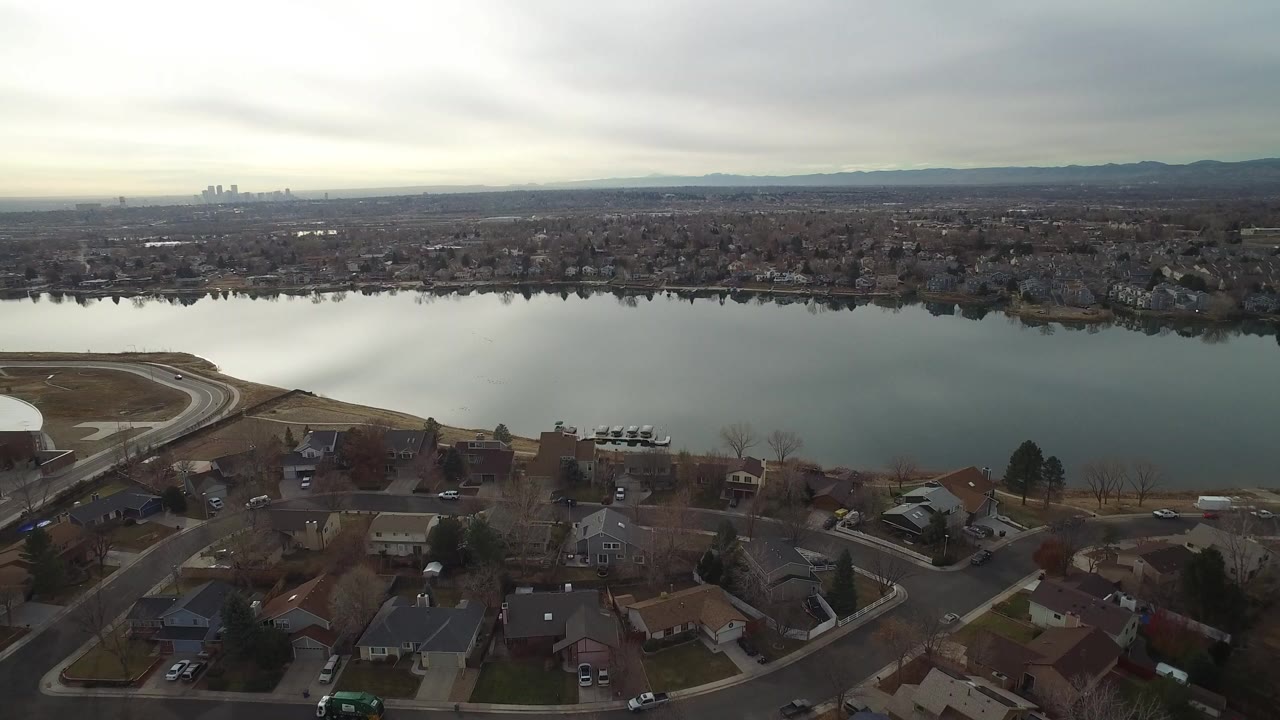 Second frame holds the Westminster, Colorado aerial view with foreground houses, a curving road near the water, and the far city skyline softened by haze, no visible people.