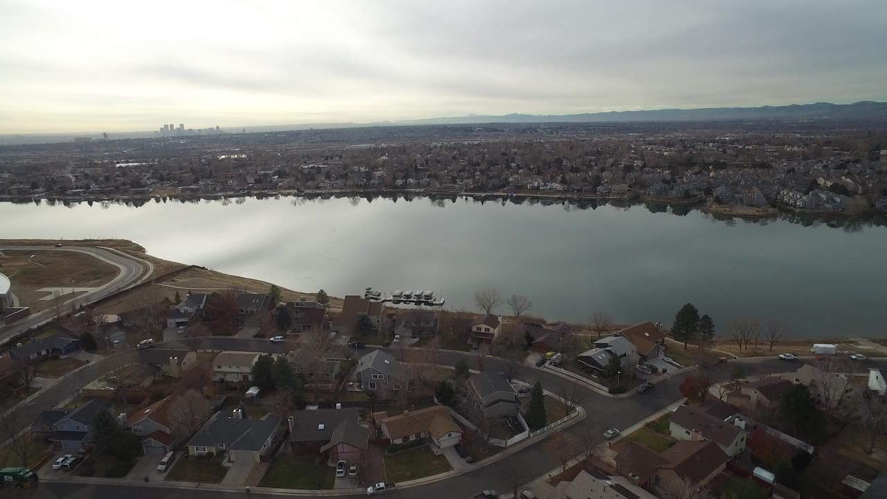 Aerial view of homes and streets beside a wide lake under gray sky.